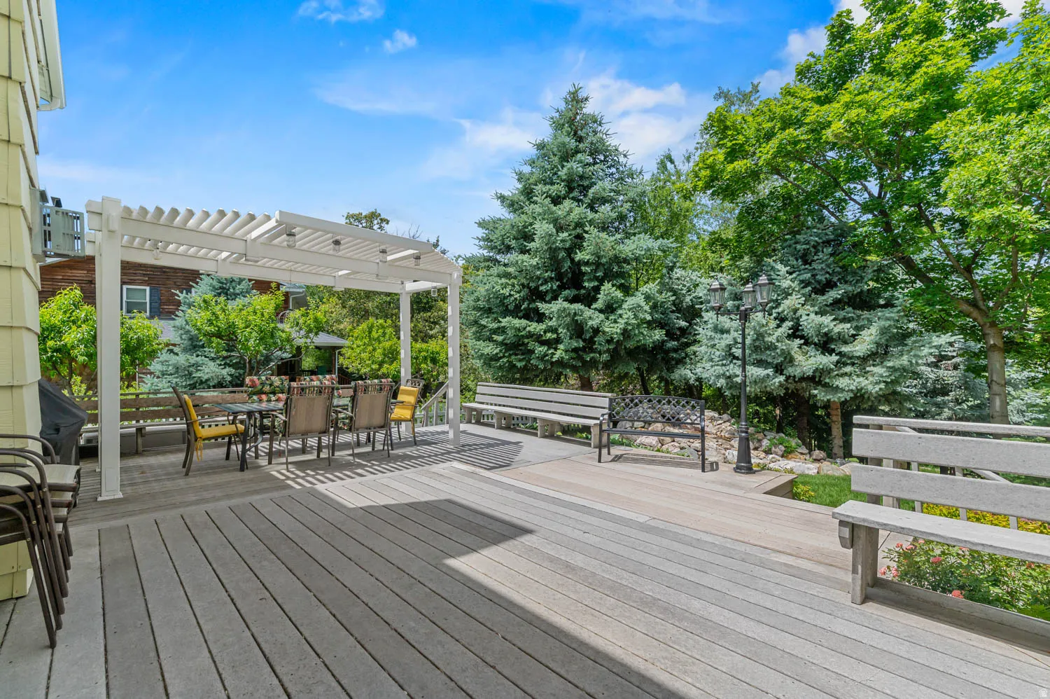 Expansive multi-level composite decking featuring a white pergola, built-in benches, and mature landscaping