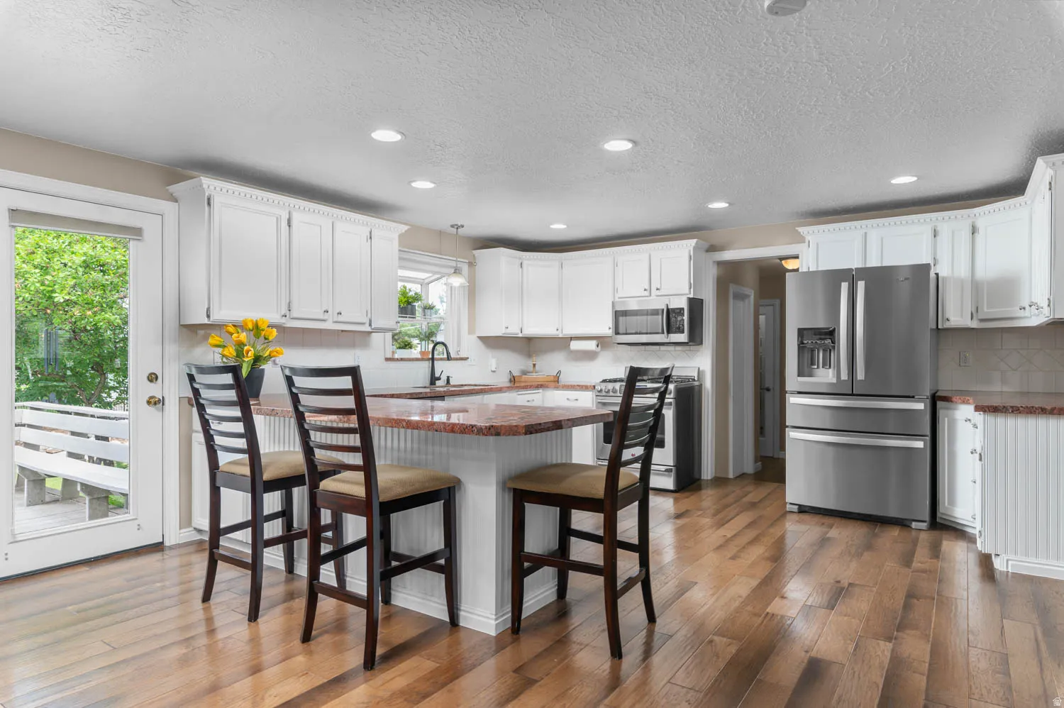 Kitchen featuring wood-finish flooring, white cabinetry with crown molding, stainless steel appliances, a center island with a stone countertop, and recessed lighting