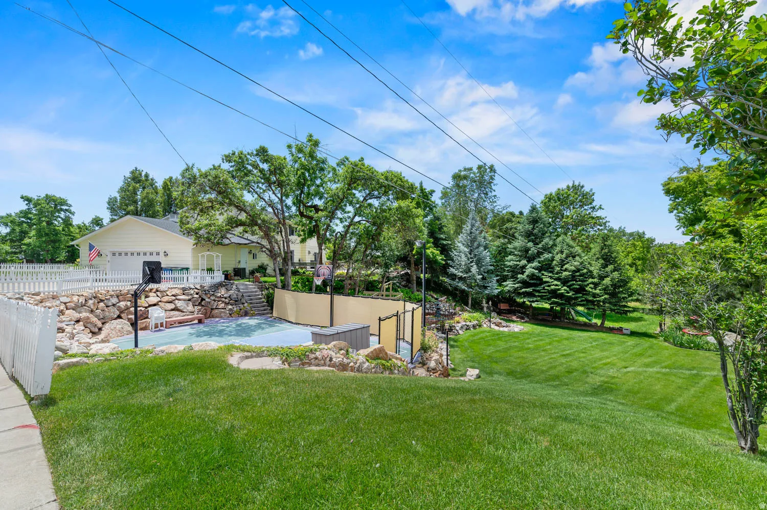 Expansive outdoor space featuring a half-court sports court, a stone retaining wall, and a verdant lawn area