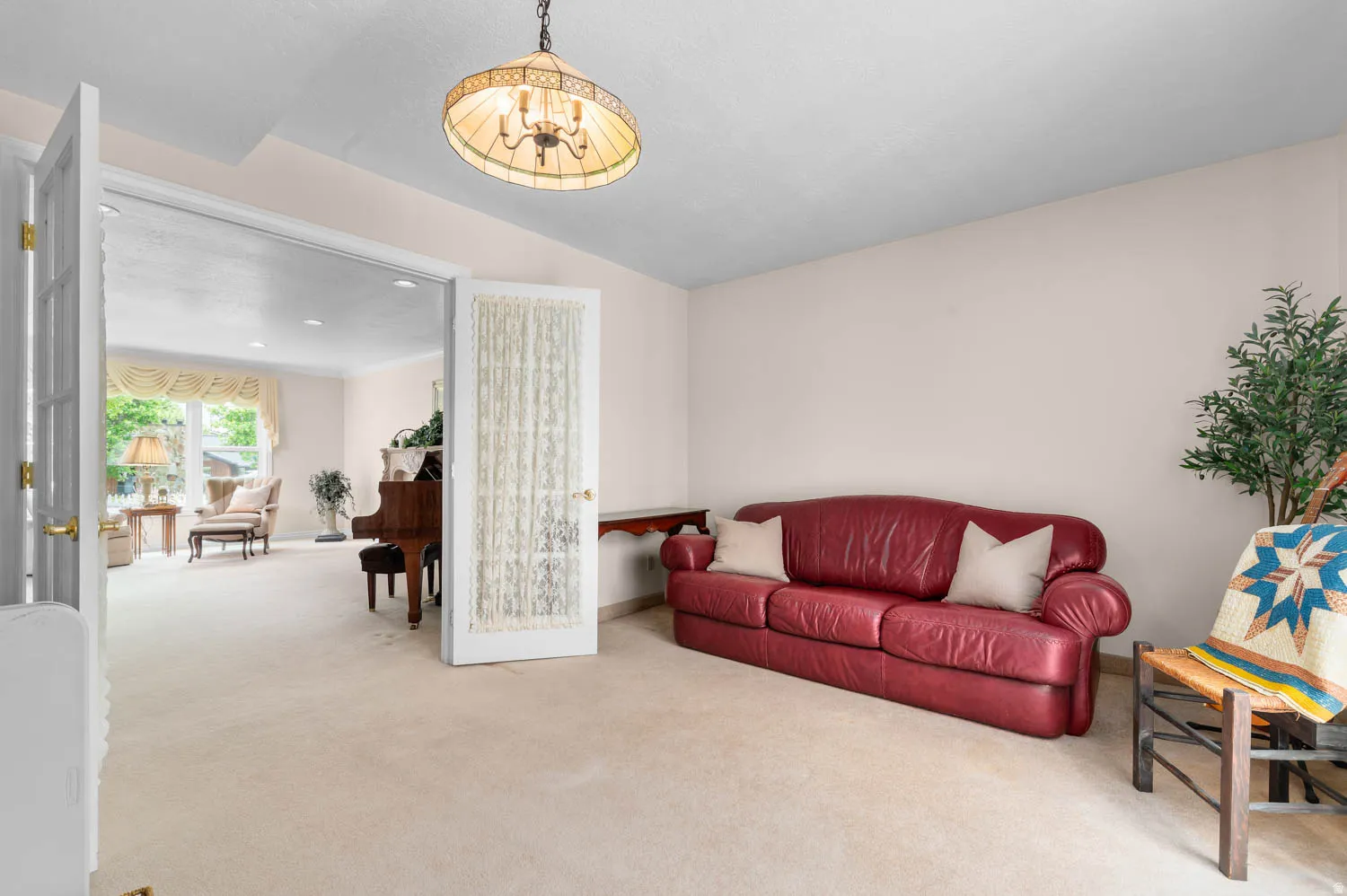 White French doors opening into a carpeted interior space with a chandelier light fixture