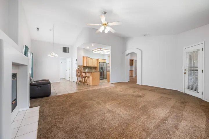 Spacious living area featuring vaulted ceilings, a built-in fireplace with a tiled hearth, and carpeted flooring
