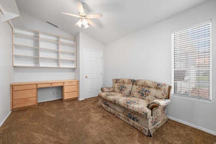 Room featuring built-in shelving and desk, textured brown carpeting, and a ceiling fan with integrated lighting