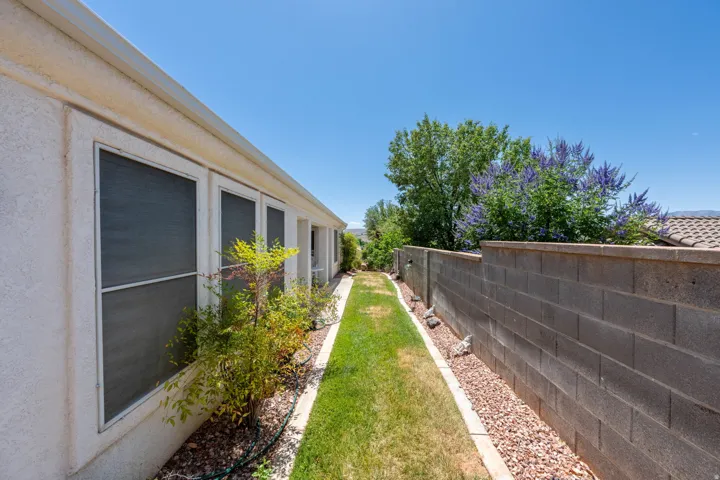 Side yard featuring a manicured grass path, decorative rock beds, and a concrete block privacy wall