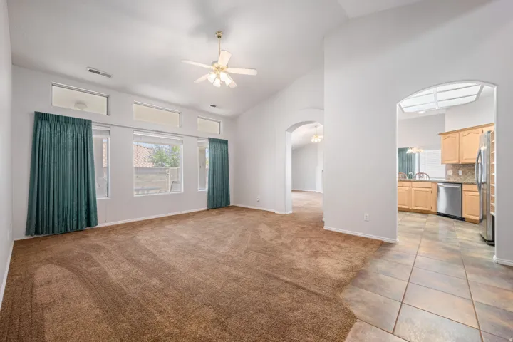 Vaulted ceiling living area with a ceiling fan, multiple windows, and transom windows