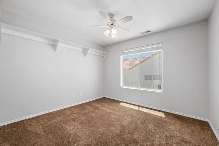 Neutral-toned room featuring a ceiling fan with integrated lighting, a large window with blinds, and white shelving along one wall