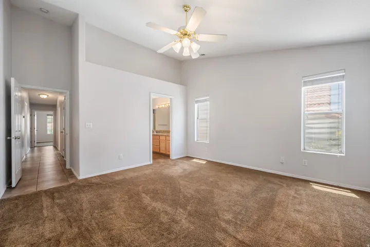 Spacious bedroom featuring vaulted ceilings, a ceiling fan, two windows, and brown carpeting
