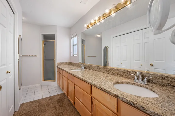 Spacious bathroom featuring a dual vanity with light-toned wood cabinetry and stone countertops