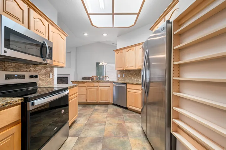 Kitchen featuring wood cabinetry, stainless steel appliances, granite countertops, a tiled backsplash, and multi-toned tile flooring