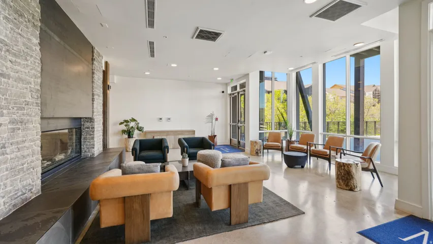Contemporary common area featuring a stone fireplace, expansive windows, concrete flooring, and recessed lighting