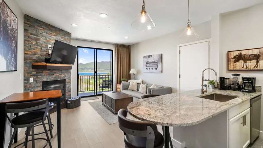 Open-concept living space featuring a stacked stone fireplace with a wood mantle, sliding glass doors to a balcony, and light wood-finish flooring