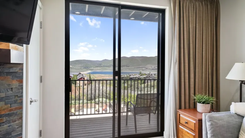 Sliding glass door leading to a balcony with black metal railings, overlooking a lake and distant mountains