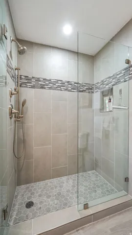 Walk-in shower featuring a frameless glass enclosure, a built-in shower niche, and a mosaic tile accent band