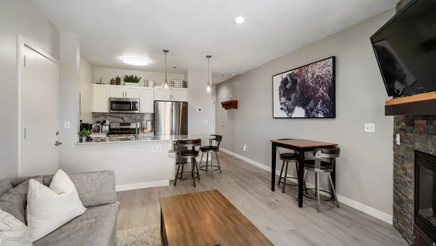 Open concept living area featuring wood-finish flooring, a kitchen with stainless steel appliances, a stone-clad fireplace, pendant lighting, and a breakfast bar
