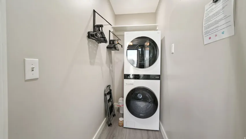 Dedicated laundry area featuring a stacked washer and dryer, a built-in hanging rod, overhead shelving, and wood-finish flooring