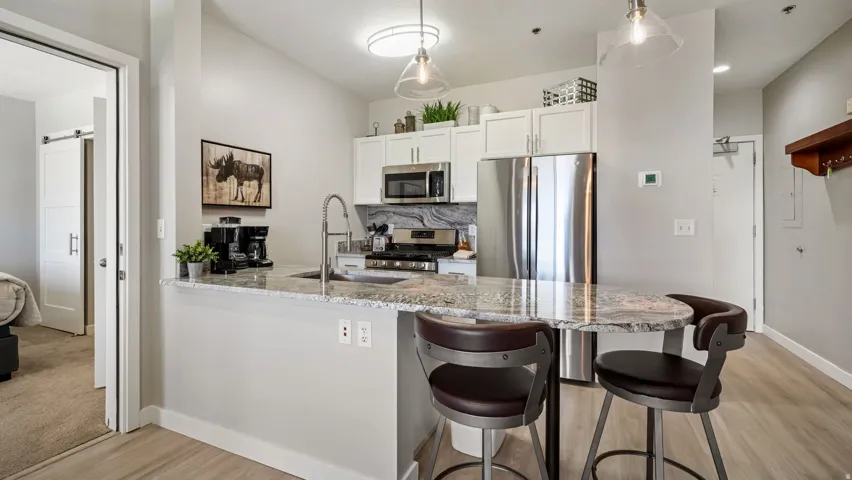 Modern kitchen featuring white cabinetry, stainless steel appliances, a stone countertop with an integrated sink, and pendant lighting