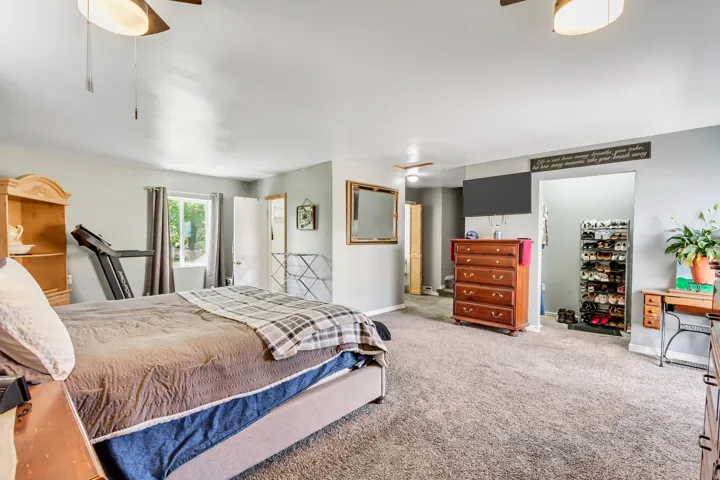 Spacious room featuring neutral carpeting, a large window with drapes, light gray wall tones, and ceiling fan light fixtures