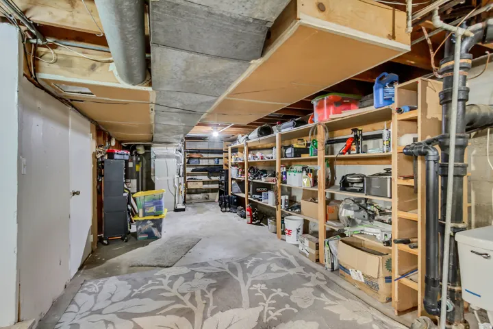Basement utility space featuring concrete flooring, exposed overhead ductwork, and extensive built-in wooden shelving for storage