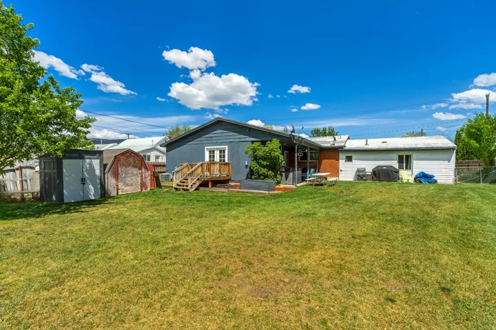 Expansive backyard featuring a lush lawn, two storage sheds, a wooden deck, and a covered patio area