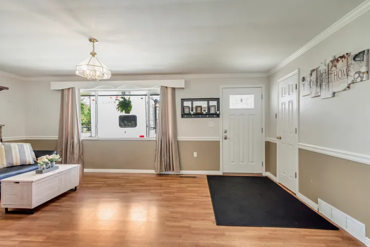 Entryway and living area featuring wood-finish flooring, a decorative chandelier, and crown molding
