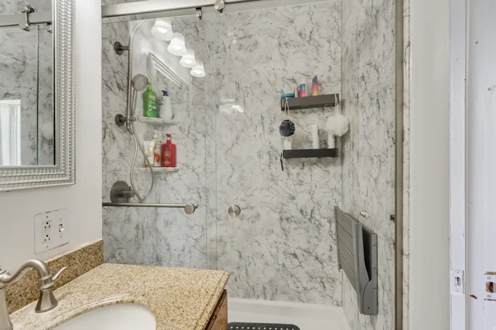 Walk-in shower with a glass enclosure, marble-style wall panels, handheld shower fixture, and built-in grab bar