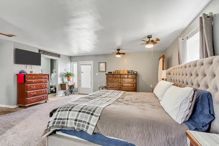Carpeted room with light gray walls, two ceiling fans, a window with curtains, and a doorway