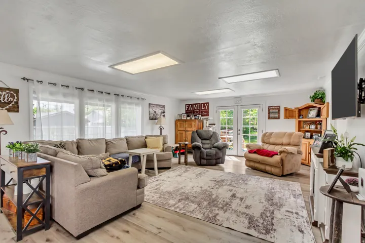 Spacious living area featuring wood-finish flooring, multiple windows providing natural light, and dual French doors