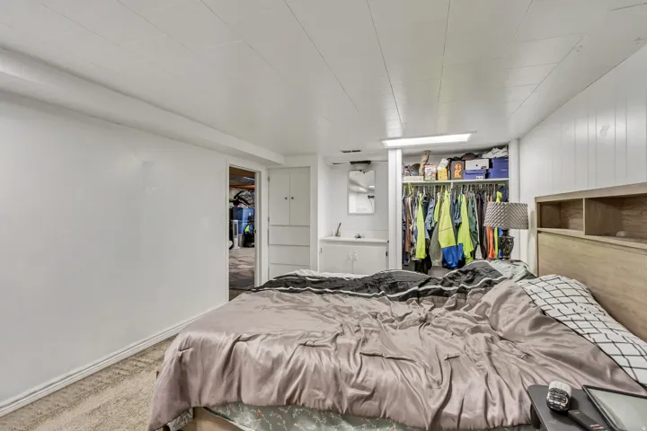 Carpeted room featuring a built-in open closet with shelving, wood-finish headboard with integrated shelving, white paneled walls, and a built-in vanity with a sink and mirror