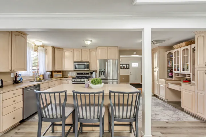Spacious kitchen featuring a central island, light wood-finish cabinetry, stainless steel appliances, and wood-finish flooring
