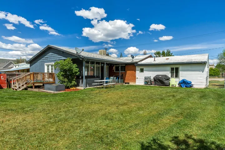 Expansive backyard with a manicured lawn, featuring a wooden deck with railing, an accessible ramp, and a covered patio area