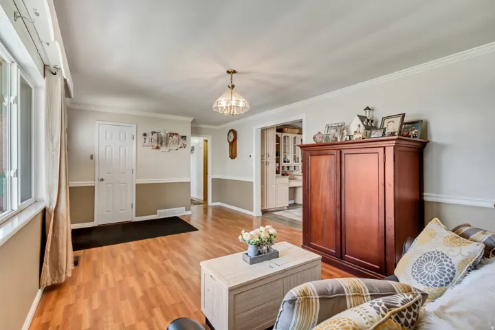 Spacious living area featuring wood-finish flooring, two-tone wall paint with crown molding, and a traditional chandelier