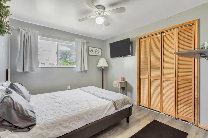 Bedroom with a ceiling fan, wall-mounted television, and wood-finish flooring