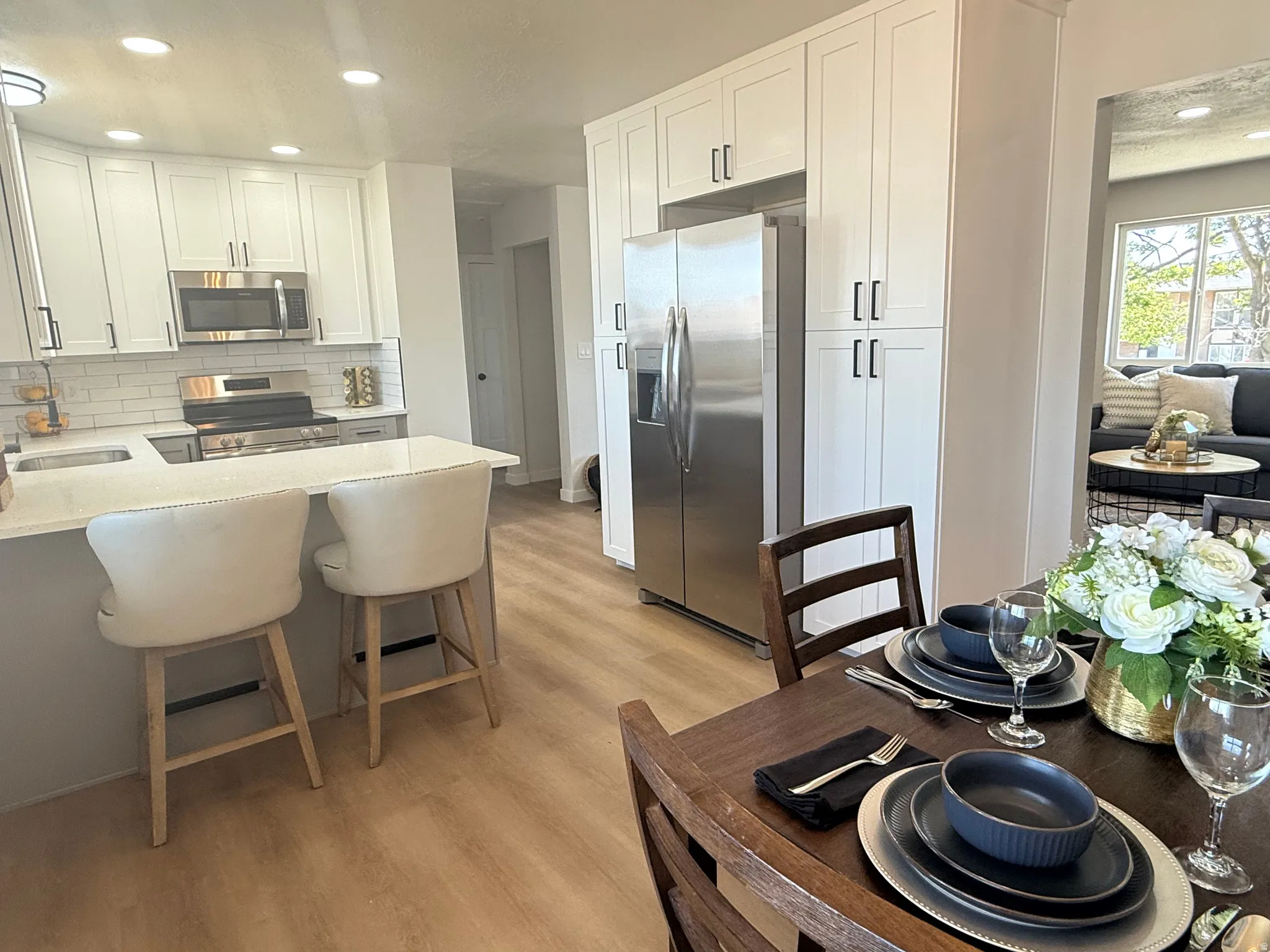 Modern kitchen featuring white shaker cabinetry, stainless steel appliances, a white subway tile backsplash, and light wood-finish flooring