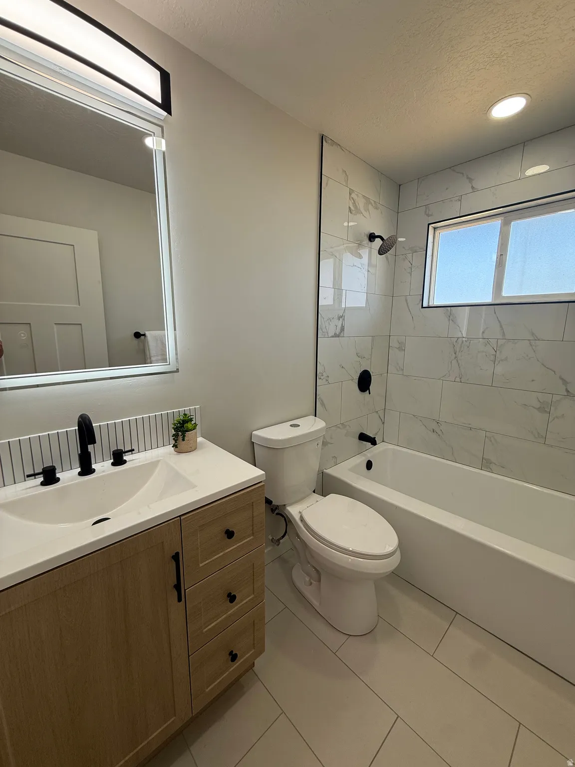 Bathroom featuring a light wood-finish vanity with a white countertop and integrated sink, matte black fixtures, and a subway tile backsplash