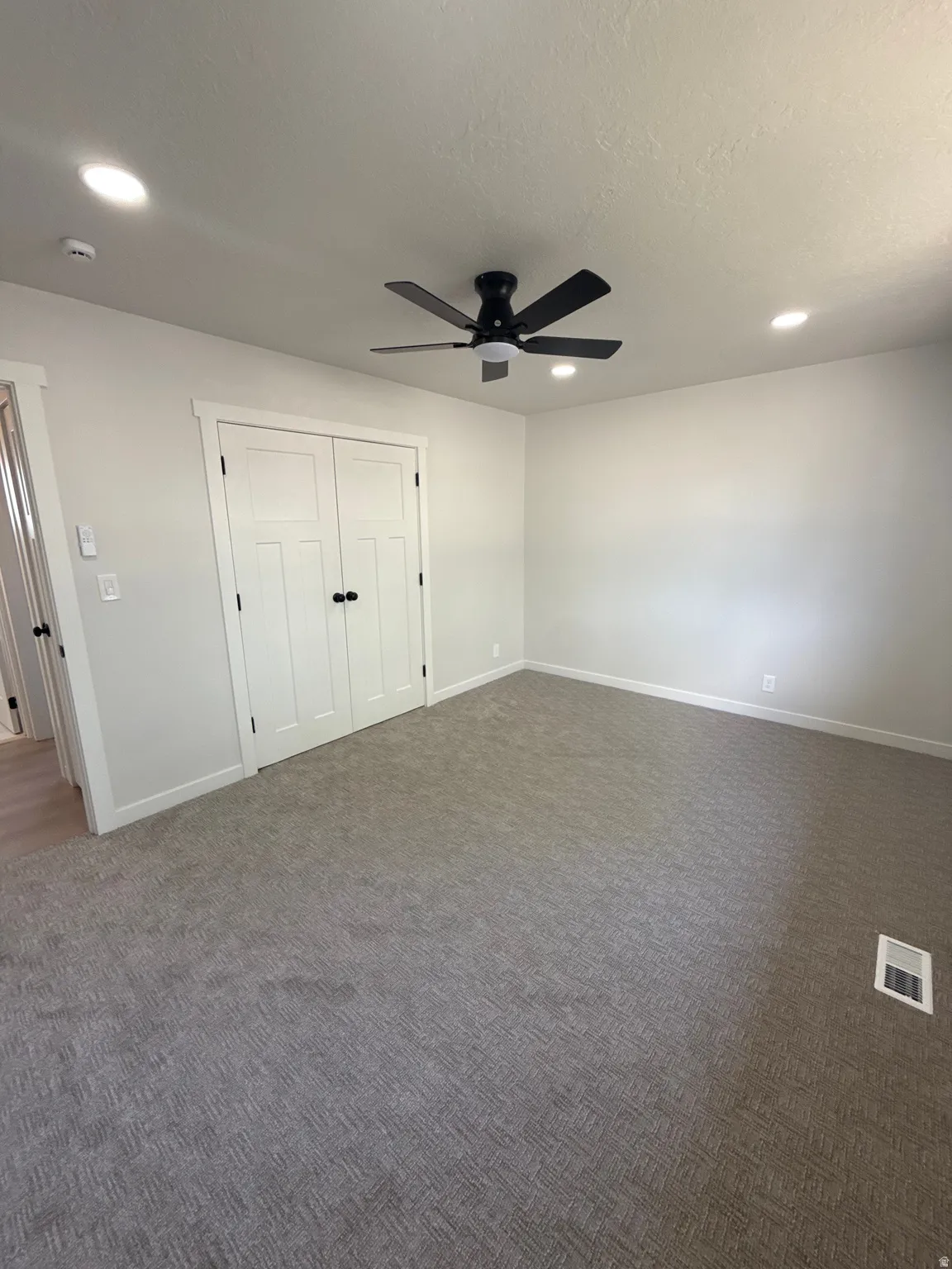 Spacious room featuring neutral carpeting, a dual-door closet with black hardware, and a black ceiling fan with integrated lighting
