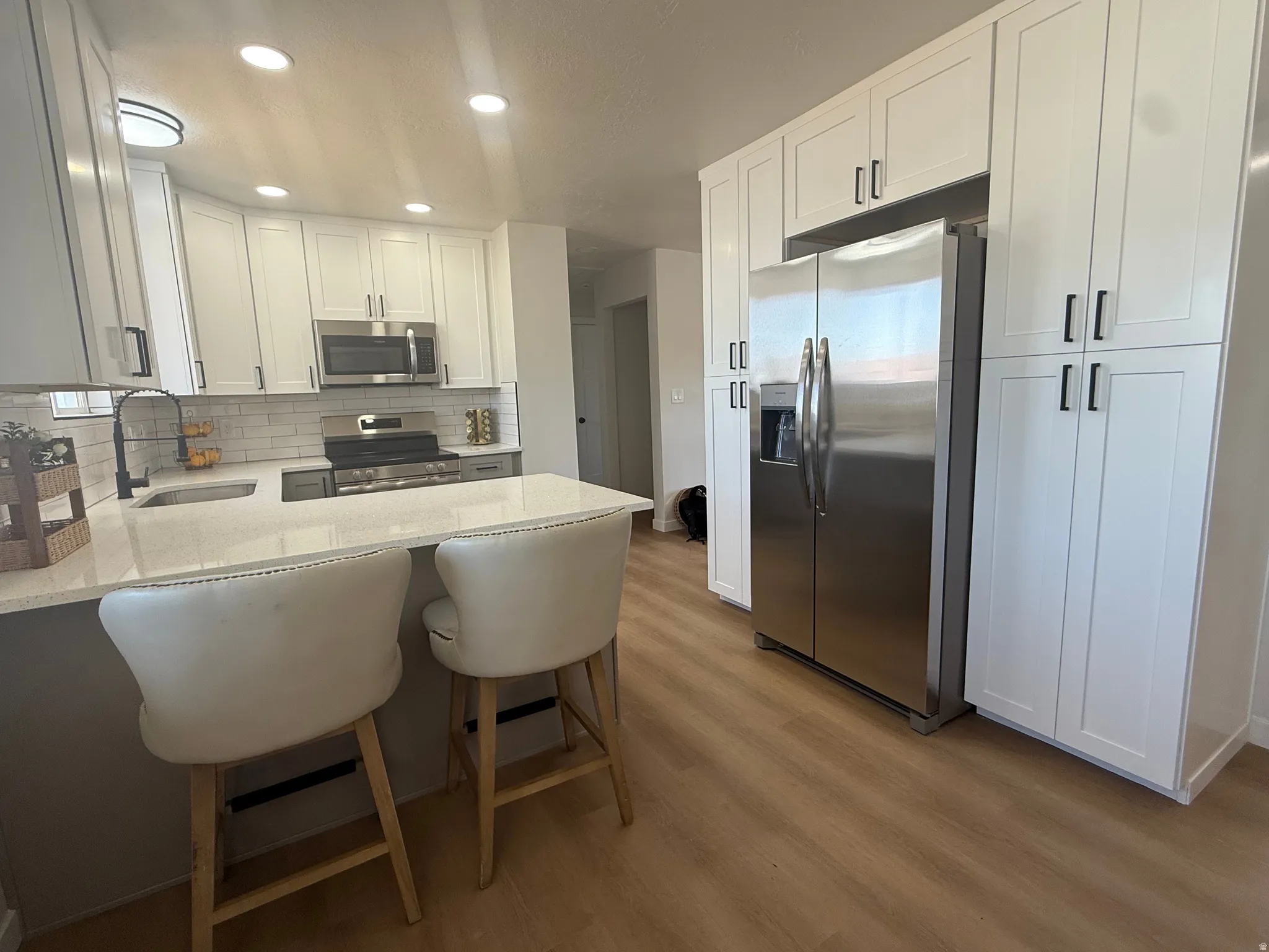 Modern kitchen featuring white shaker-style cabinetry, stainless steel appliances, light-toned countertops, subway tile backsplash, and wood-finish flooring