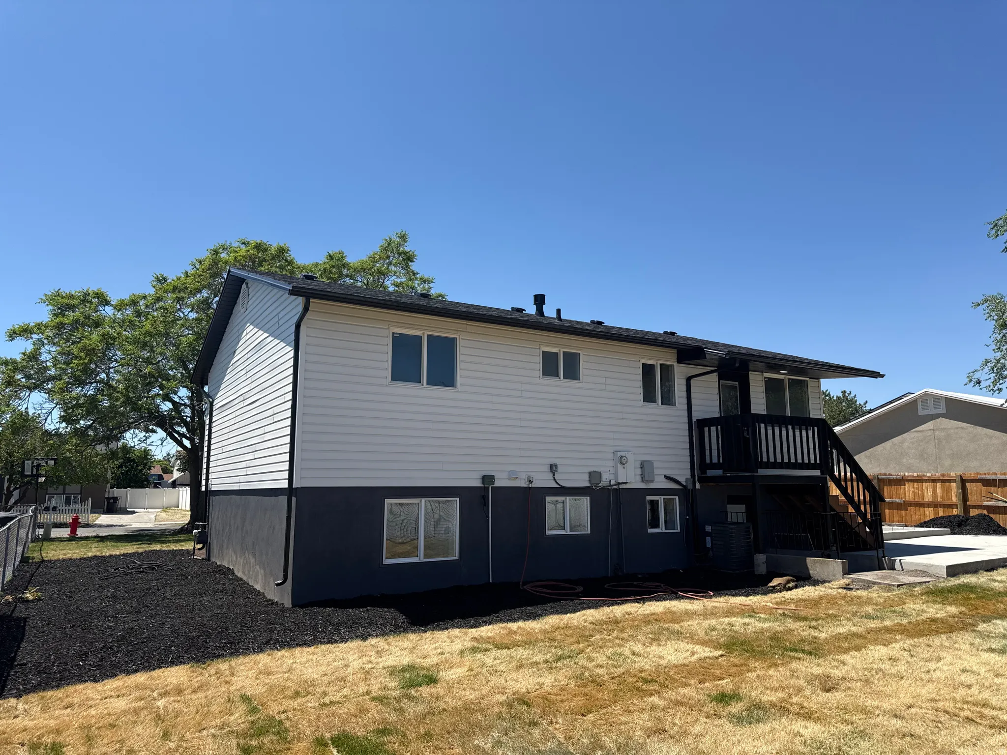 Rear exterior featuring white horizontal siding, a black painted foundation, and a black deck with stairs