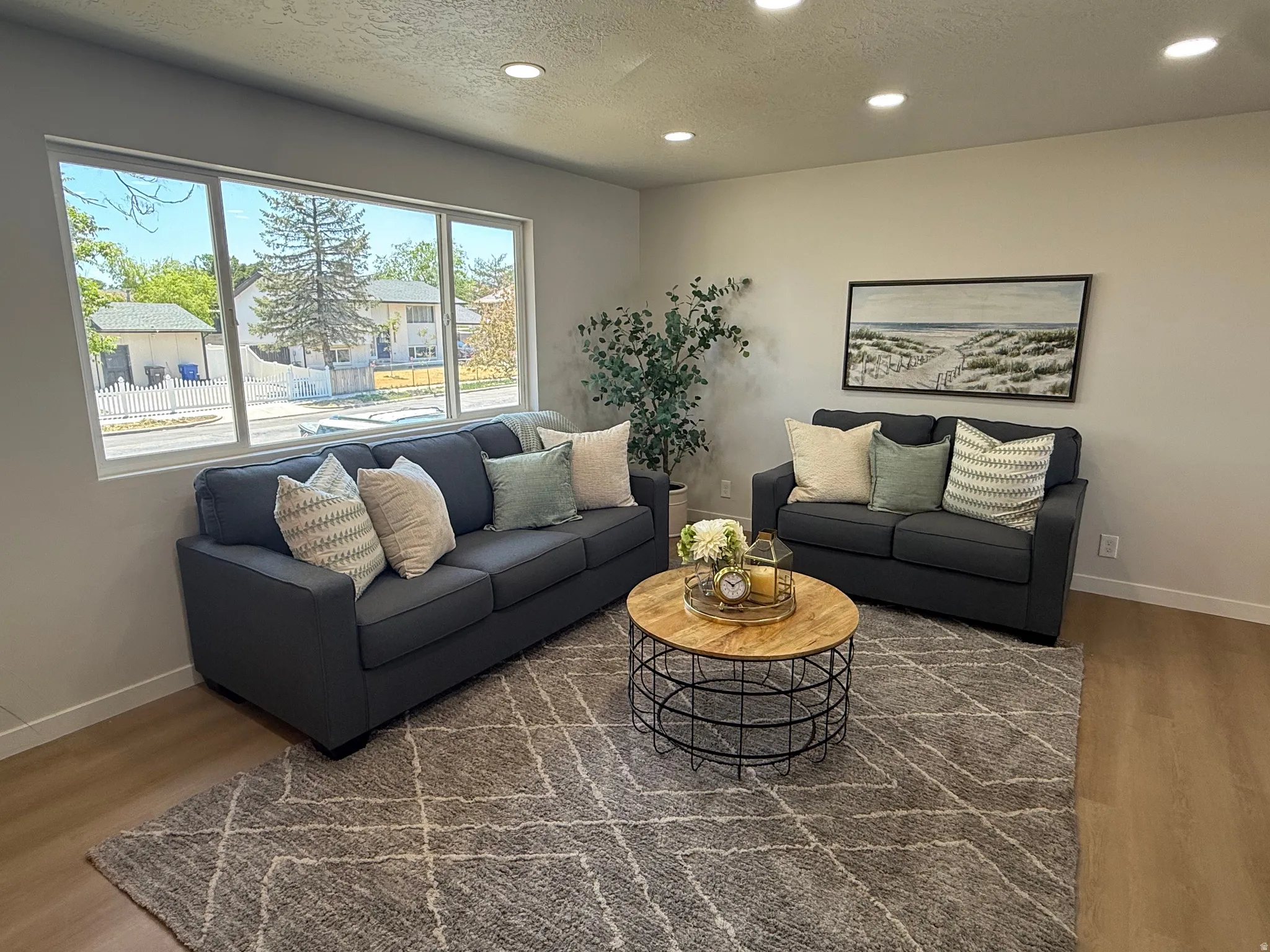 Bright living area featuring large windows, recessed lighting, neutral wall tones, wood-finish flooring, and a patterned area rug