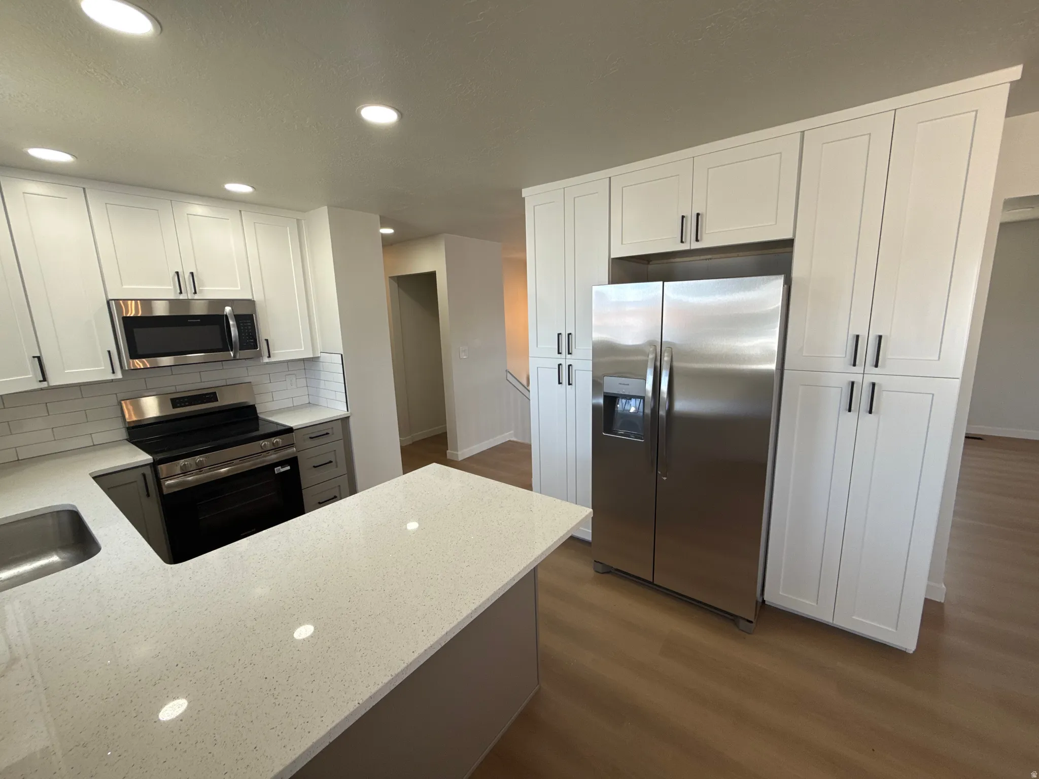 Open-concept kitchen featuring white shaker cabinetry, stainless steel appliances, and a built-in refrigerator