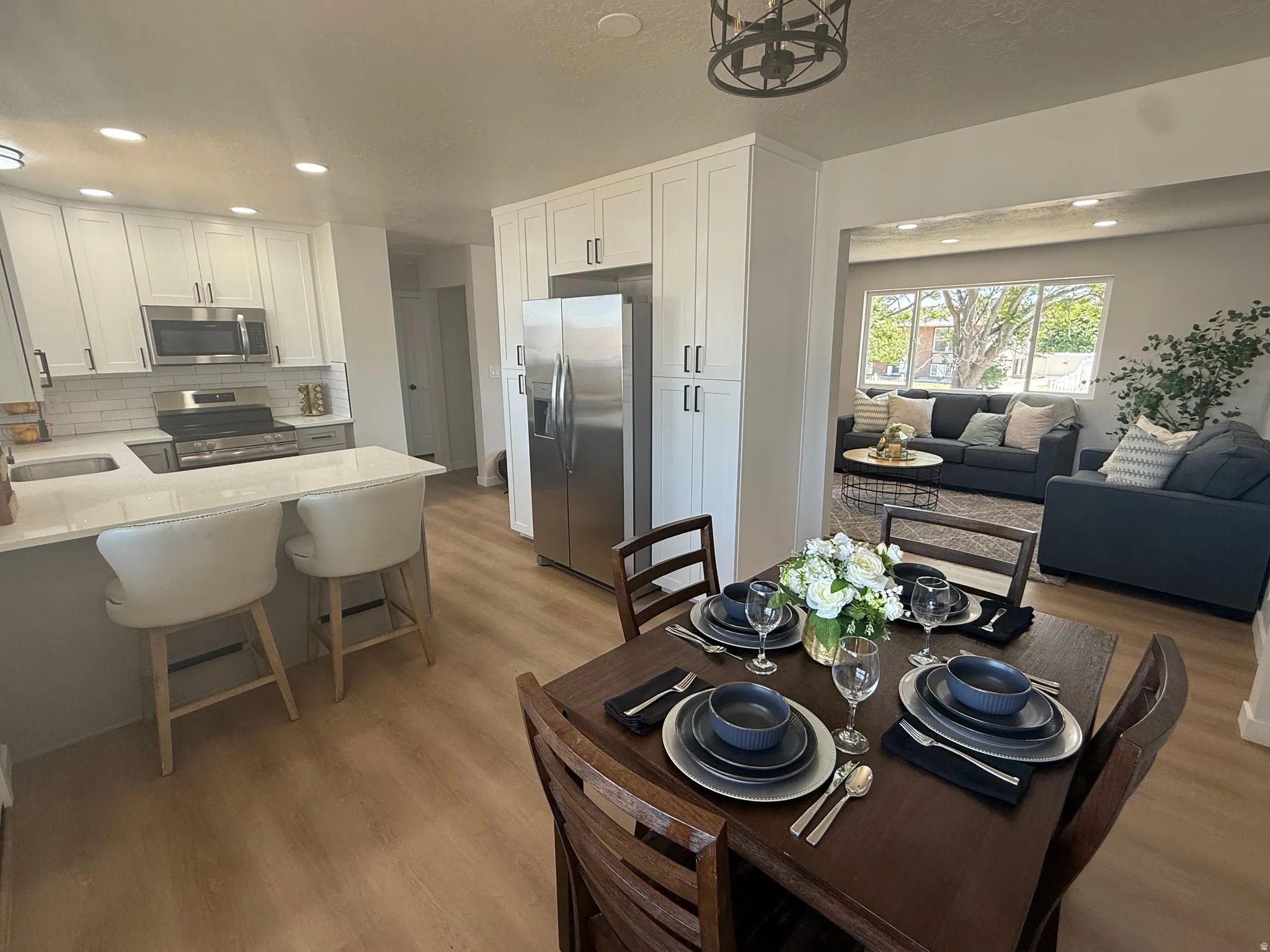 Open-concept dining area with wood-finish flooring, a kitchen island with seating, white shaker cabinetry, stainless steel appliances, and recessed lighting