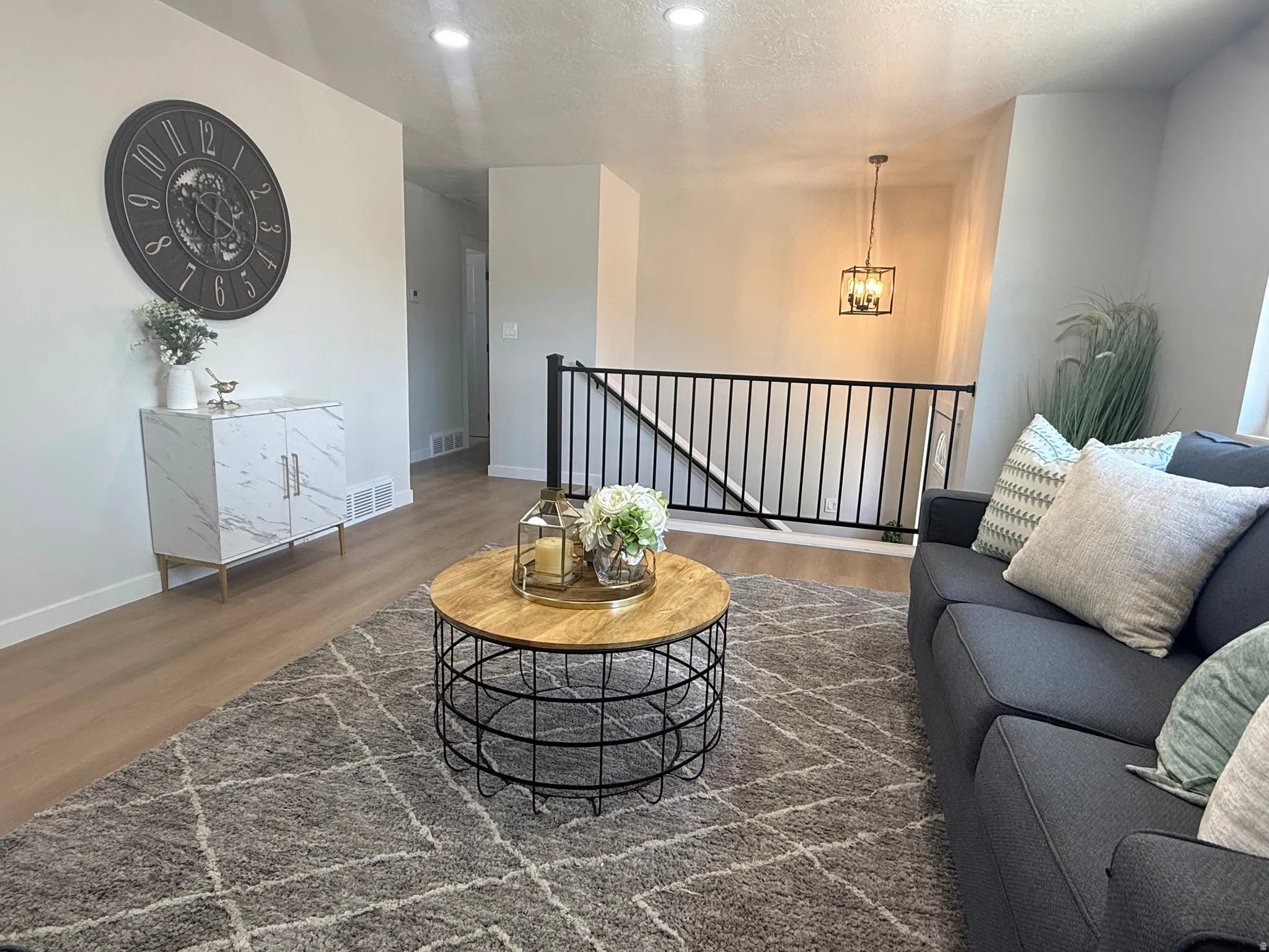Open-concept living area featuring wood-finish flooring, recessed lighting, and a black metal staircase railing