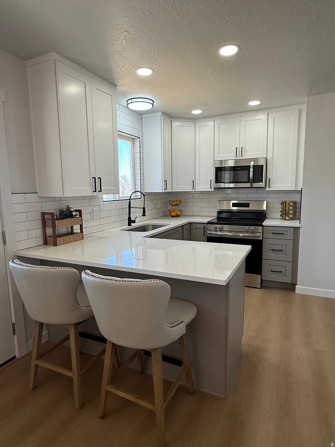 Modern kitchen with light wood-finish flooring, white upper cabinetry, and gray base cabinetry