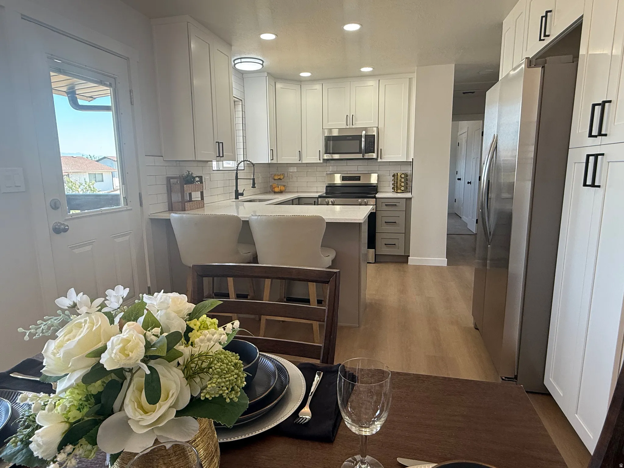 Modern kitchen featuring white shaker cabinetry, stainless steel appliances, a subway tile backsplash, and light wood-finish flooring