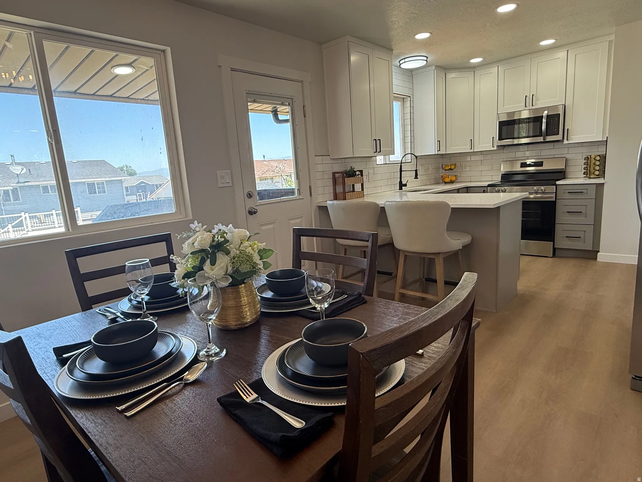 Open-concept kitchen and dining area featuring light-finish flooring, white shaker cabinetry, stainless steel appliances, a white subway tile backsplash, and a breakfast bar with seating