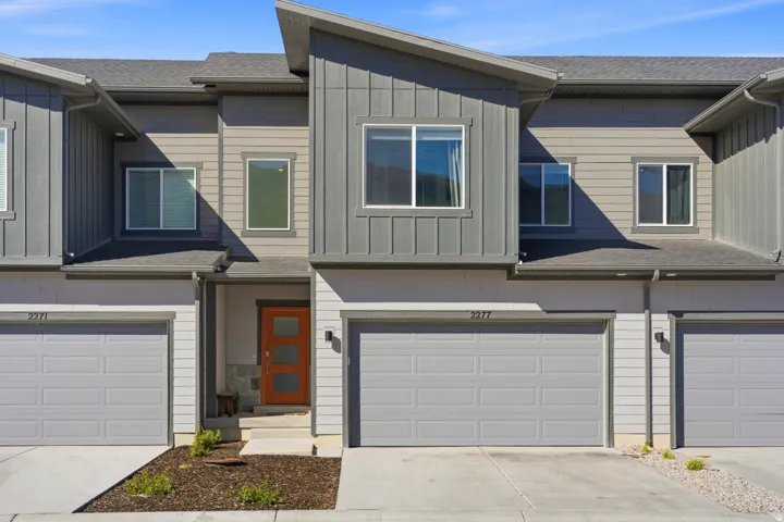 Contemporary townhome exterior featuring an orange wood-panel entry door with frosted glass inserts, a single-car garage, and a modern asymmetrical roofline