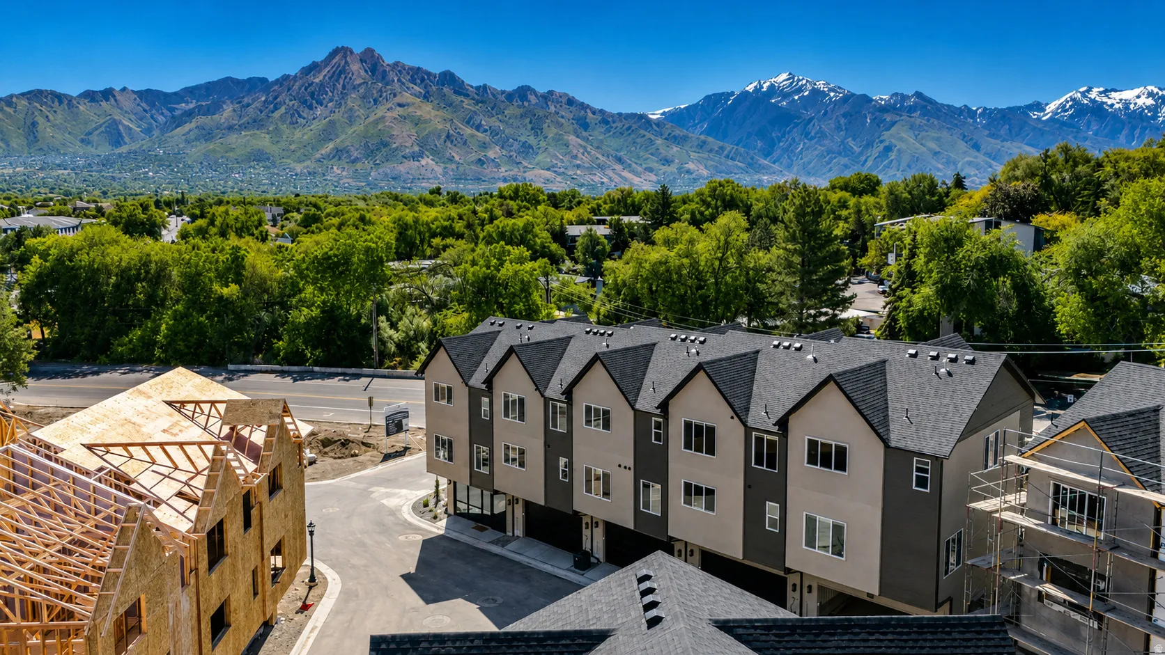 Modern townhome development with a combination of light and dark exterior finishes, prominent gabled roofs, and a paved street