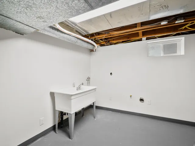 Utility room featuring a freestanding utility sink with chrome faucet, painted concrete flooring, and exposed ceiling joists
