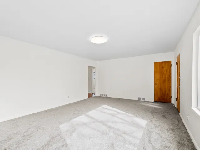 Bright room with light gray carpeting, white walls, a flush-mount ceiling light, natural wood-finish interior doors, and white window trim