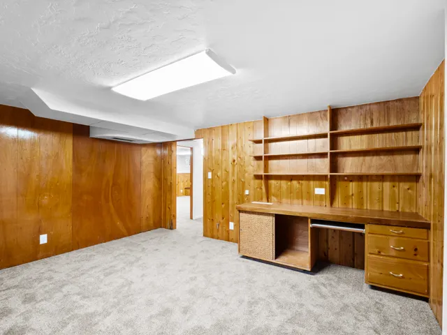Room featuring wood-paneled walls, light grey carpet, and a white textured ceiling