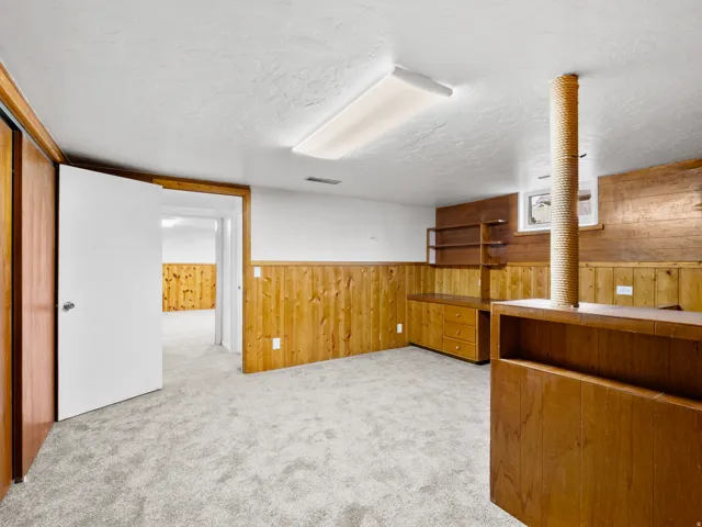 Carpeted room featuring wood-paneled walls, built-in shelving, a built-in wooden cabinet with drawers, and an open doorway