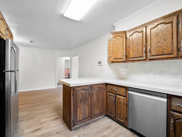 Kitchen featuring wood cabinetry, white countertops, tile backsplash, and stainless steel appliances
